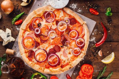 Taze ve ham malzemelerle çevrili ahşap bir masada duran salamlı ve sebzeli lezzetli pizza.