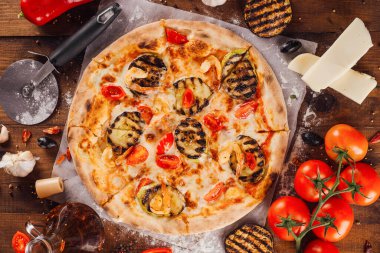 Tahta bir masada taze malzemelerle çevrili karides ve ızgara patlıcanlı lezzetli pizza.