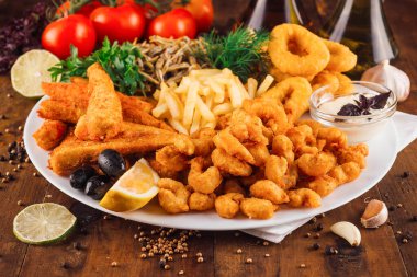 Ahşap masada patates kızartması servis edilen büyük bir tabak lezzetli deniz ürünü.