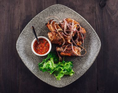 Kırmızı soğanlı ızgara domuz kaburgası ve soslu otlar ve koyu ahşap arka planda taze marul.