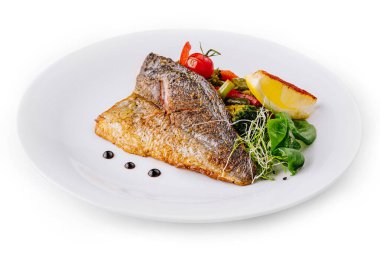 Izgara balık filetosu beyaz bir tabakta sebze, limon ve otlarla servis edilir.