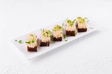 Krem peynirli ve yeşillikli nefis kanepeler beyaz bir tabakta yatıyor.