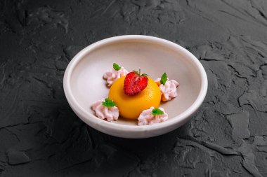 Mango panna cotta çilek, nane ve kremayla süslenmiş bir tabakta servis edilir.