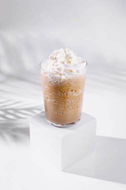 Creamy iced coffee beverage topped with whipped cream, sitting on white cube with palm leaf shadows clipart