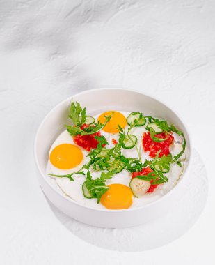 Beyaz tabakta servis edilen roka, domates ve salatalıklı yumurta.