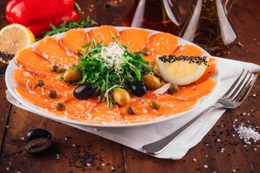 Taze roka, zeytin, limon ve ahşap restoran masasında servis edilen kapari ile süslenmiş somon carpaccio aperatifi.