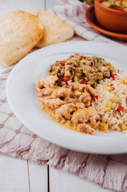 Pilavlı tavuk, patlıcan salatası ve arka planda kilden bir çömlek bulunan beyaz kırsal masa üzerindeki ekmek sağlıklı bir ev yemeğini temsil ediyor.