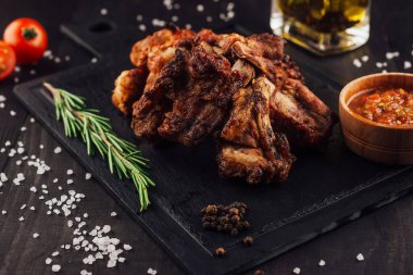 Lezzetli ızgara domuz pirzolası, siyah taşın üzerinde, baharat, biberiye, tuz ve sos ile kesilmiş, koyu ahşap masa üzerinde.