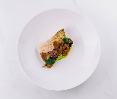 Lezzetli ve güzel kaplanmış balık tabağı, ızgara balık, sotelenmiş mantar ve canlı yeşil bir sos içeren beyaz bir tabakta servis edilir.