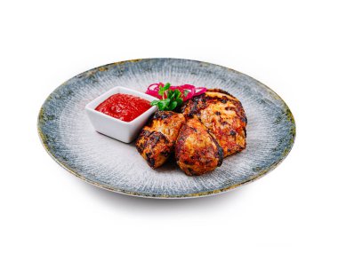 Izgara tavuk butları kırmızı soslu, otlu ve soğanlı bir tabakta servis edilir.