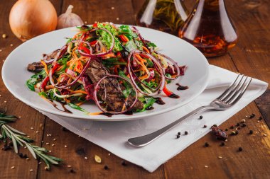 Izgara biftekli sıcak salata ve beyaz tabakta servis edilen balzamik soslu taze sebzeler.