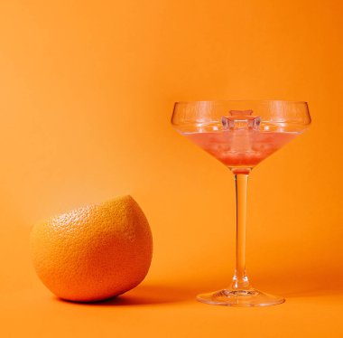 Tazeleyici greyfurt kokteyli turuncu bir arka planda duruyor ve yanında da greyfurt var.