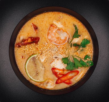 Baharatlı Thai Tom çorbası siyah bir kasede servis edilir.