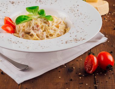 Zarif beyaz bir tabakta servis edilen kremalı carbonara makarnası taze fesleğen ve kiraz domatesleriyle süslenmiş.