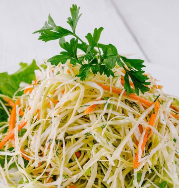 Parçalanmış beyaz lahana, rendelenmiş havuç ve beyaz tabakta dereotu ile taze salata, ahşap masada servis edilir.