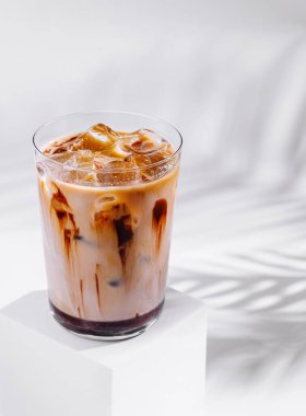 Bir bardak ferahlatıcı buzlu kahve beyaz küpün üzerinde duran gölgeli beyaz arka planda çikolata şurubu.