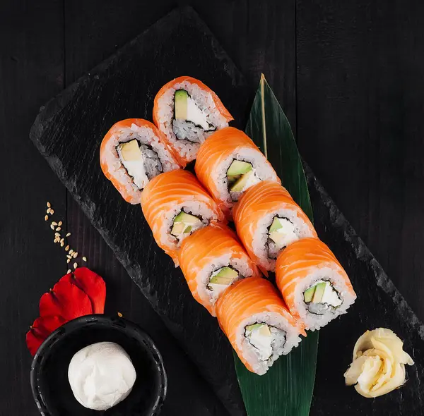 Somon, avokado ve krem peynirli siyah taş tabakta Philadelphia suşi rulosu.