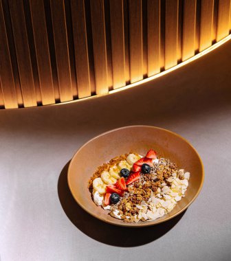 Bir masada yoğurt, çilek, yabanmersini ve muz dilimli granola tabağı servis edilir.