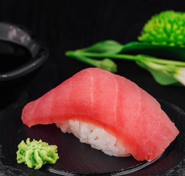 Taze ton balıklı nigiri suşi. Siyah taş bir tabakta servis ediliyor. Wasabi ve soya soslu. Çiçeklerle süslenmiş.