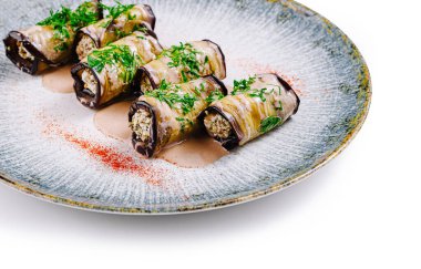 Sos ve baharatla süslenmiş tabakta fındık ve otlarla doldurulmuş lezzetli patlıcan ruloları var.