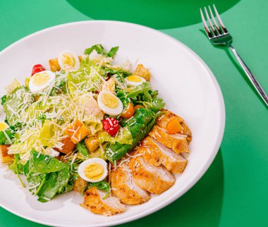 Taze ve lezzetli sezar salatası ızgara tavuk göğsü, kızarmış ekmek, parmesan peyniri ve bıldırcın yumurtası, beyaz tabakta servis edilir.