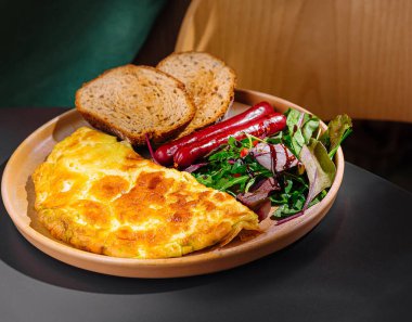 Omlet, sosis, tost ve salata ile nefis kahvaltı tabağı, masada servis edilir.