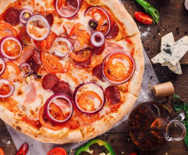 Domatesli lezzetli pizza, kırmızı soğan, jambon ve salam ahşap masada malzemelerle birlikte.