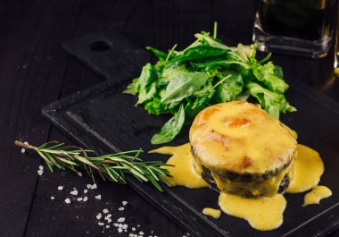 Siyah taş tabakta duran, limon ve otlarla süslenmiş peynir soslu leziz kızarmış balık.