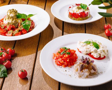 Variety of tomato and cheese dishes artfully presented on white plates, with rustic wood table backdrop