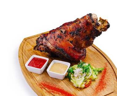 Ahşap tahtada servis edilen sulu kızarmış domuz budu soslu ve beyaz arka planda salata.