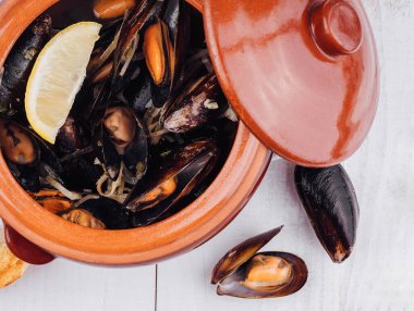 Lezzetli deniz ürünleri, beyaz ahşap masadaki kil çömlekte haşlanmış midyeler.