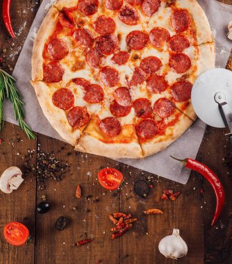 Köy ahşap masadaki malzemelerle çevrili taze pişmiş pepperoni pizzası.