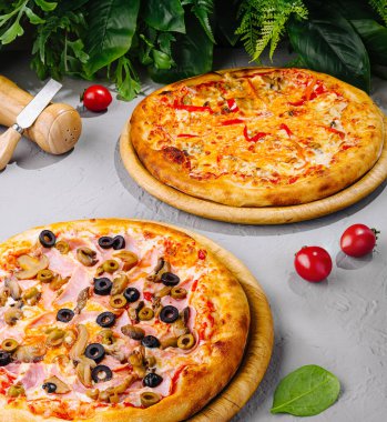 Erimiş peynirli ve ahşap tahtalarda duran farklı malzemeli iki farklı pizza.