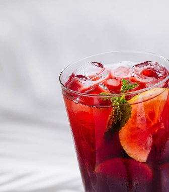 Limonlu ve naneli bir bardak buzlu çay beyaz arka planda duruyor.