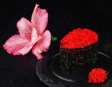 Siyah arka planda pembe çiçekle süslenmiş kırmızı havyar tobiko ile Gunkan maki sushi