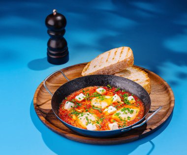 Bir tavada Shakshuka, yanında kızarmış ekmek dilimleri ve maydanozla servis edilir.