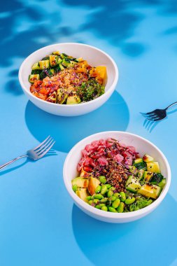 Parlak mavi arka planda iki canlı ve renkli kase servis edilir. Sağlıklı ve lezzetli bir yemek sergilenir.