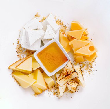 Beyaz arka planda servis edilen farklı peynir, bal ve ceviz çeşitlerine sahip tabak.