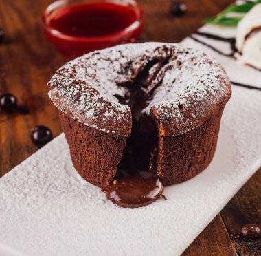 Beyaz bir tabağa erimiş çikolata damlatan çikolatalı pasta, bir kepçe vanilyalı dondurma, böğürtlen ve çikolata ile servis edilir.