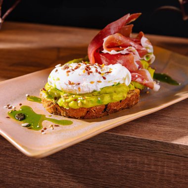 Avokado püresi ve jambon ve tohumla süslenmiş zeytinyağı serpiştirilmiş haşlanmış yumurta.