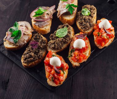 Lezzetli bruschetta, domatesler, mozarella, et ezmesi ve ringa balığı siyah taş kesme tahtasının üzerinde.