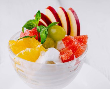 Dondurma, kırmızı elma dilimleri, yeşil üzümler, portakal dilimleri ve greyfurt dilimleri gibi taze meyveli cam bir tatlı kasesinde servis ediliyor.