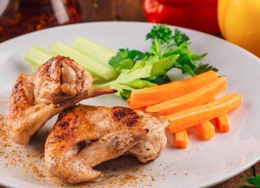 Lezzetli kızarmış tavuk kanatları, kereviz ve havuç çubuklarıyla servis edilmiş ahşap tabakta, mükemmel bir öğle yemeği fikri.