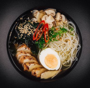 Lezzetli bir kase ramen çorbası tavuk, mantar, yumurta ve yeşillikle servis ediliyor.