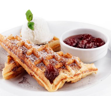 Çilek reçelli waffle 'lar ve dondurma beyaz bir tabağa serpilmiş, çikolata serpiştirilmiş.