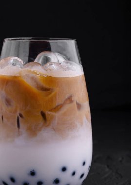 Siyah arka planda süt ve boba toplarıyla karıştırılmış ferahlatıcı buzlu kahve dolu bardaklar.