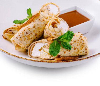 Süzme peynirli ince krepler ve nane yapraklarıyla süslenmiş muz dilimleri beyaz tabakta tatlı soslu.