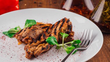 Beyaz tabakta ızgara tavuk göğsü. Ahşap masada yeşil salata servis ediliyor.