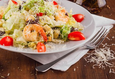 Karidesli Sezar salatası ahşap bir masada beyaz bir tabakta servis edilir.