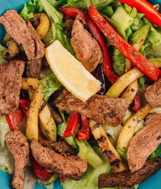 Izgara sığır eti dilimli sıcak salata ve biber ve limon suyuyla baharatlı kabak gibi kızarmış sebzeler.